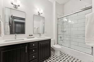 Bathroom featuring bath / shower combo with glass door and double vanity