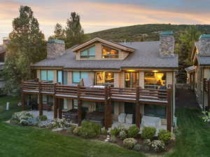 Back of property at dusk with a chimney, a deck, and a lawn