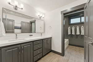 Bathroom featuring double vanity, light wood finished floors, a bath, and a textured wall