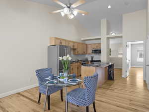 Dining space with high vaulted ceiling, light wood-style flooring, and a ceiling fan