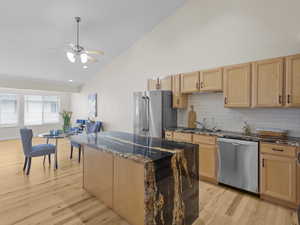 Kitchen with light brown cabinetry, decorative backsplash, dark stone countertops, appliances with stainless steel finishes, and light wood-type flooring