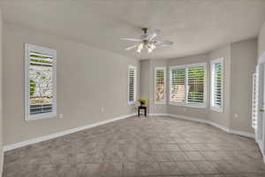 Unfurnished room with ceiling fan, light tile patterned floors, and a textured ceiling