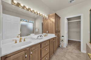 Full bathroom with double vanity, a spacious closet, and light tile patterned floors