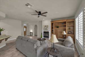 Living area featuring a tile fireplace, light tile patterned flooring, arched walkways, and a ceiling fan