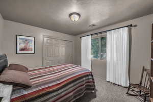 Bedroom with a textured ceiling, light carpet, and a closet