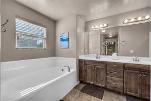 Bathroom featuring plenty of natural light, double vanity, a garden tub, a textured ceiling, and light tile patterned flooring
