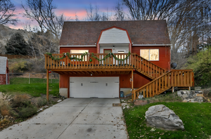 Back of house with a wooden deck, concrete driveway, an attached garage, stairs, and a lawn