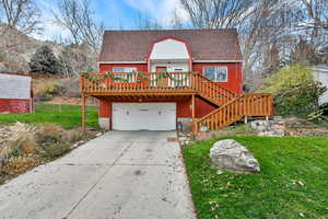 Chalet / cabin with a wooden deck, concrete driveway, stairs, an attached garage, and roof with shingles