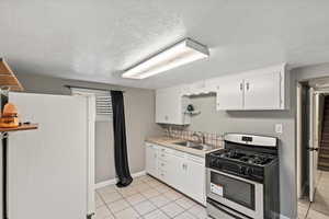 Kitchen featuring stainless steel gas range oven, freestanding refrigerator, white cabinets, light tile patterned floors, and a textured ceiling