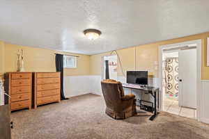 Office area featuring a textured ceiling, light carpet, and wainscoting