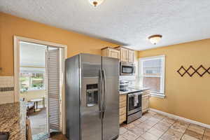 Kitchen featuring appliances with stainless steel finishes, a textured ceiling, light brown cabinets, light stone countertops, and light tile patterned flooring