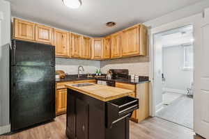 Kitchen with wooden counters, black appliances, marble backsplash, light wood-style flooring, and a center island