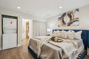 Bedroom with wood finished floors, stacked washer/dryer, and recessed lighting.