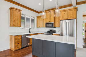 Kitchen with a kitchen island, decorative light fixtures, appliances with stainless steel finishes, dark wood-type flooring, and light stone countertops