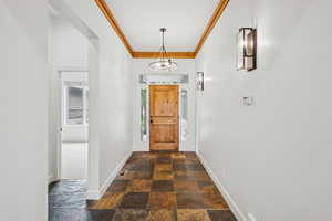 Hallway with crown molding, dark stone finish flooring, and a chandelier