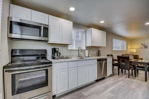 Kitchen with stainless steel appliances, white cabinets, light stone counters, and recessed lighting