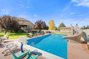 View of pool with a patio, a water slide, and fenced backyard.
