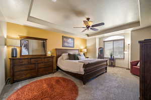 Bedroom featuring a tray ceiling, carpet flooring, ceiling fan, and a textured ceiling