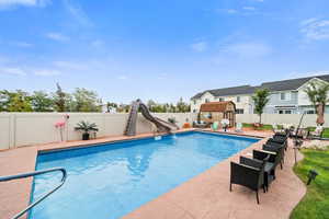 View of pool with a fenced backyard, a water slide, a patio area, and a storage unit