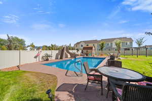 View of swimming pool with a patio area, a fenced backyard, & outdoor dining space
