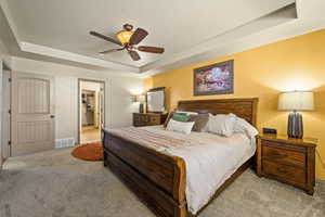 Bedroom featuring a raised ceiling, carpet, ceiling fan, and ensuite bathroom