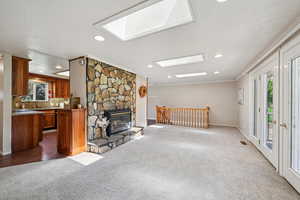 Unfurnished living room featuring dark carpet, a skylight, recessed lighting, and a stone fireplace
