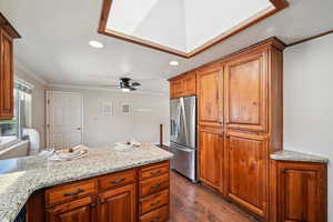 Kitchen featuring recessed lighting, light stone countertops, crown molding, dark wood-type flooring, and stainless steel refrigerator with ice dispenser