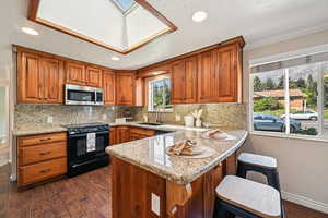 Kitchen featuring dark wood finished floors, brown cabinetry, a peninsula, light stone countertops, and recessed lighting