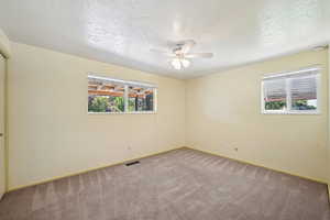 Carpeted empty room featuring a textured ceiling and a ceiling fan