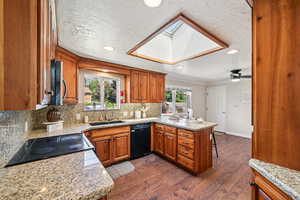 Kitchen with tasteful backsplash, brown cabinetry, dark wood-style flooring, a peninsula, and a skylight