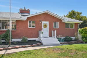 View of front of house featuring brick siding, a front yard, and a chimney