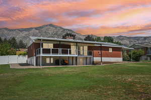 Back of property at dusk featuring a mountain view, a lawn, and a chimney