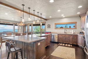 Kitchen featuring a kitchen bar, decorative light fixtures, beam ceiling, light stone counters, and a textured ceiling