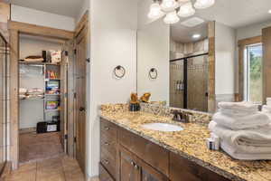 Bathroom with a walk in closet, a shower stall, vanity, light tile patterned floors, and a textured ceiling