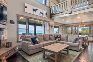 Living room with a chandelier, hardwood / wood-style floors, a stone fireplace, and a high ceiling