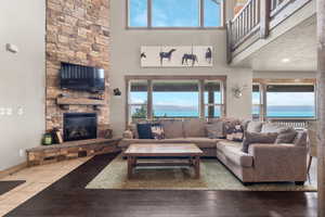 Living area with a stone fireplace, plenty of natural light, a high ceiling, and wood finished floors
