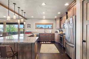 Kitchen featuring appliances with stainless steel finishes, a textured ceiling, light stone counters, a center island, and hanging light fixtures