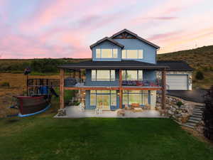 Back of house at dusk featuring a patio, a balcony, a yard, and a garage