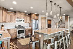 Kitchen with dark wood-style floors, stainless steel appliances, light stone countertops, pendant lighting, and recessed lighting