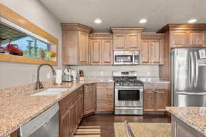 Kitchen featuring appliances with stainless steel finishes, light stone counters, dark wood finished floors, recessed lighting, and a textured ceiling