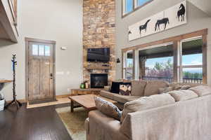 Living area with hardwood / wood-style floors, a stone fireplace, and a high ceiling