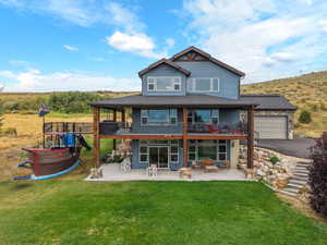 Rear view of house featuring a patio, a balcony, a lawn, stone siding, and a shingled roof