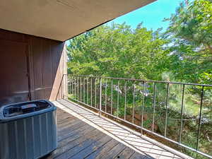 Covered private balcony surrounded by mature trees, offering outdoor living and added privacy in a top-floor unit.