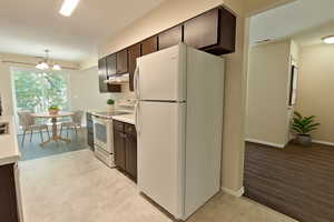 Kitchen featuring white appliances, light countertops, dark brown cabinetry, a chandelier, and a textured ceiling