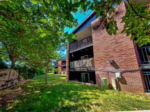 Rear view of house with a lawn, a balcony, and brick siding