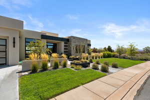 View of front of home with a front yard, stone siding, and stucco siding