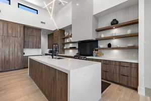 Kitchen featuring open shelves, tasteful backsplash, modern cabinets, a center island with sink, and brown cabinets