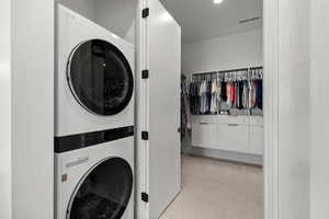 Washroom featuring stacked washing machine and dryer, light colored carpet, and recessed lighting