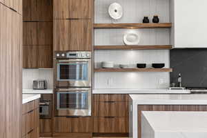 Kitchen featuring open shelves, brown cabinets, double oven, and tasteful backsplash