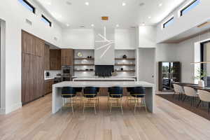 Kitchen with a high ceiling, open shelves, modern cabinets, a center island with sink, and recessed lighting